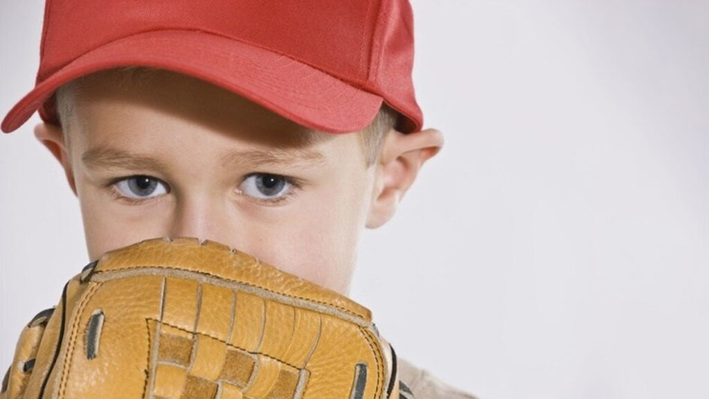 young boy wearing baseball hat and baseball glove covering his face